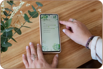 Image from brand photo shoot of fingers touching a phone on a table with a plant to the left. The phone shows a to-do list.