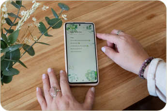 Image from brand photo shoot of fingers touching a phone on a table with a plant to the left. The phone shows a to-do list.
